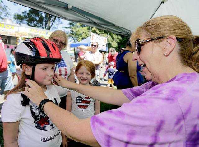 Brianna Crecy, 8, left, and her sister Kaitlyn, 7, both of Detroit, Mich. and visiting their grandparents in Pringle, get fitted for bicycle helmets by HKQ Kids' Sally Stravinski at Kirby Park on Thursday. - Bill Tarutis | For Times Leader